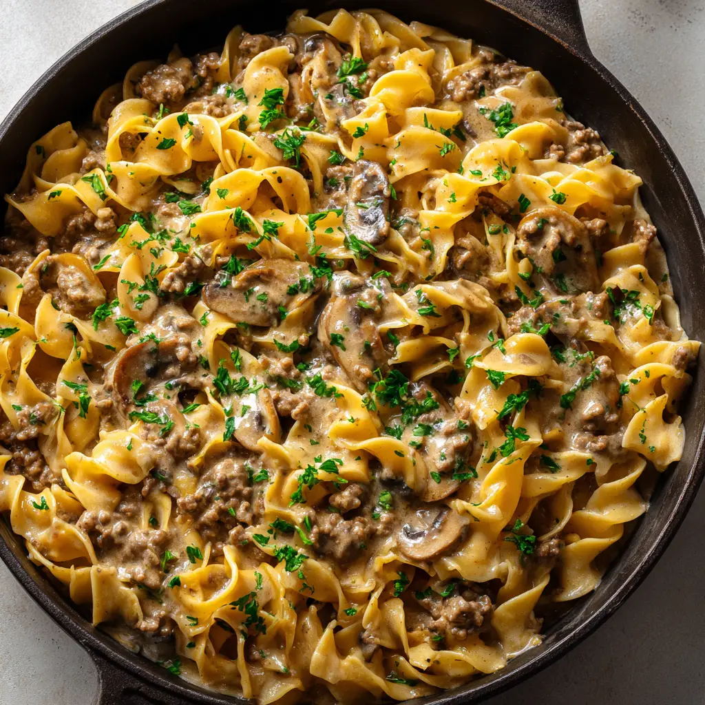 Close up showing the deeply browned ground beef crumbles and sautéed button mushrooms with slightly darkened edges resting in a thick stroganoff sauce.