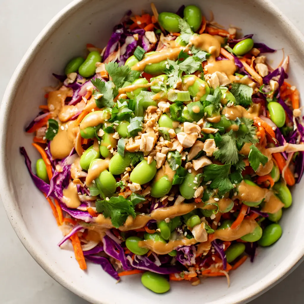 Overhead shot of shredded purple cabbage, julienned orange carrots, and bright green edamame beans in a white ceramic bowl. (Asian Edamame Salad Recipe)