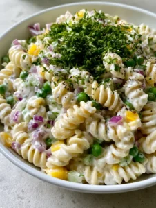 Close-up of Sour Cream Pasta Salad showing the thick white dressing, vibrant green peas, and yellow pepper cubes in a white bowl.