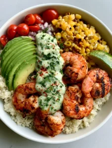 Top-down view of a Grilled Shrimp Bowl with plump pink shrimp, charred corn, and an avocado fan over white quinoa.