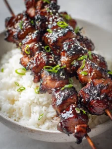 Stacked grilled chicken skewers with black char marks and thick dark brown glaze. (Huli Huli Chicken)