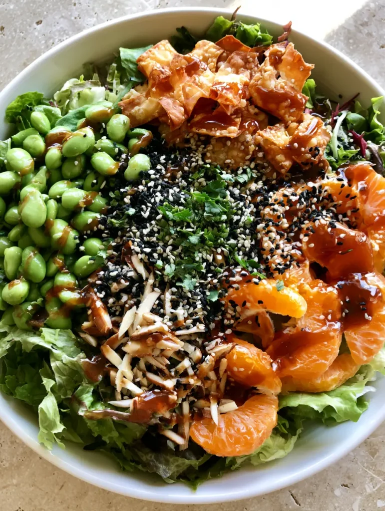 Detailed shot of mandarin orange segments and toasted almond slivers garnished with black and white sesame seeds on a bed of greens with Asian Sesame Salad Dressing.