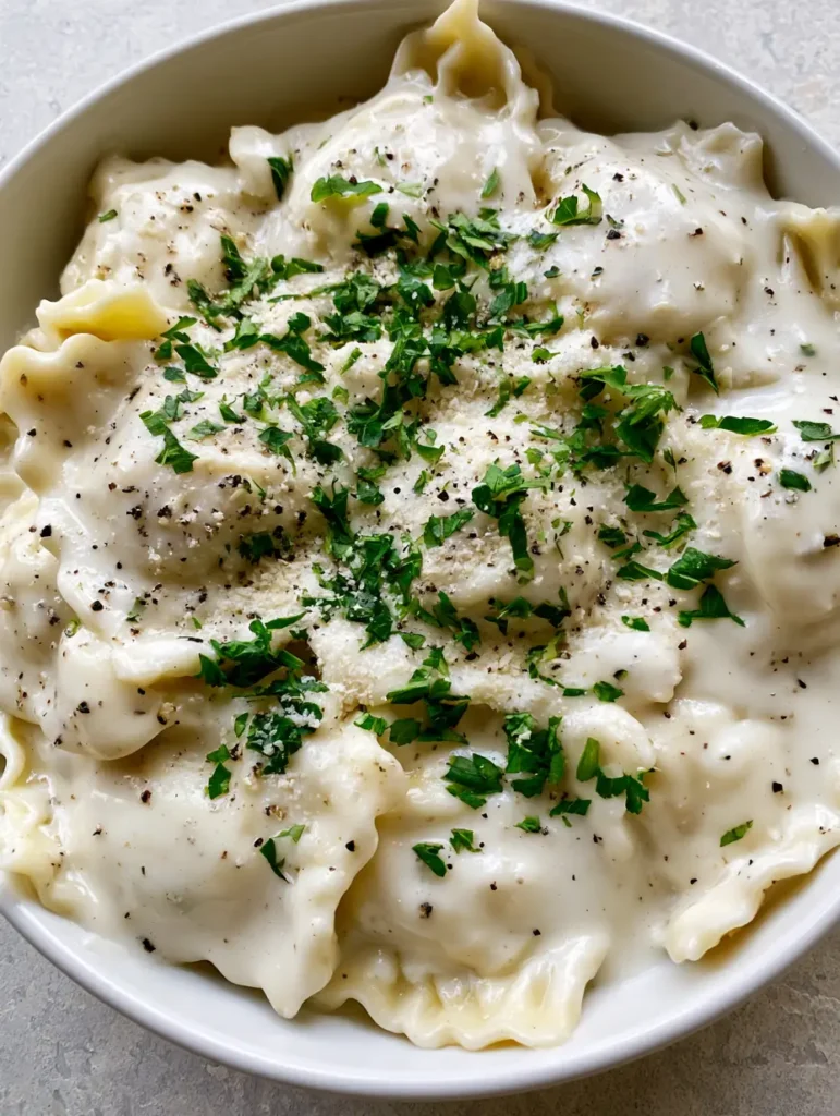 Top-down view of a white ceramic bowl with thick Garlic Parmesan Ravioli Sauce and finely grated parmesan cheese garnish.