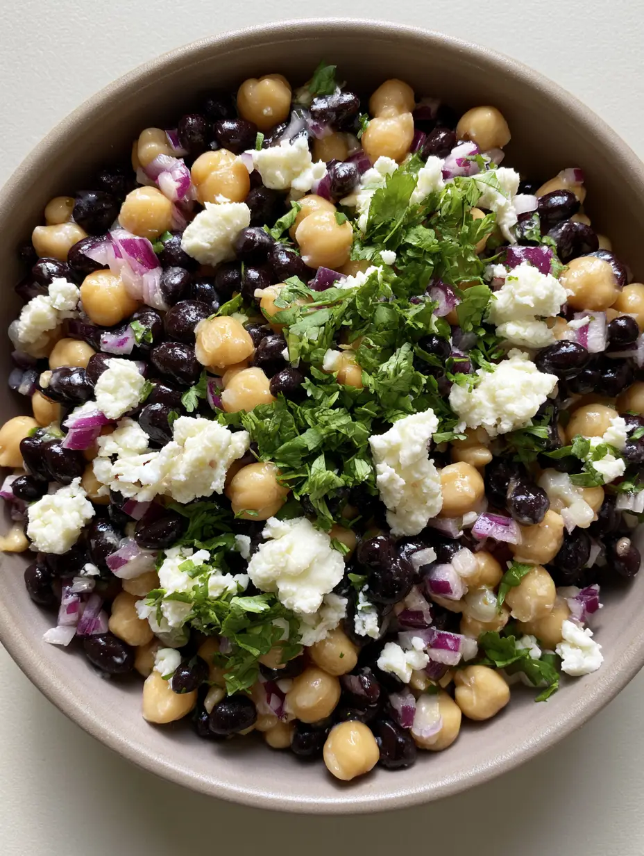Overhead view of a vibrant Chickpea and Black Bean Salad with finely diced red onion and bright green cilantro. (Chickpea and Black Bean Salad)