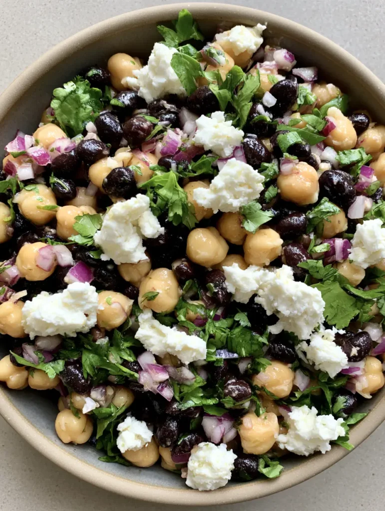 Side view of a Chickpea and Black Bean Salad in a neutral ceramic bowl showing the glistening translucent lime dressing.