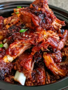Close-up of tender pork spare ribs in a black crockpot showing meat pulling away from the bone. (Crockpot BBQ Ribs)
