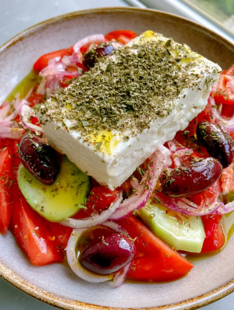 Authentic Greek Horiatiki Salad: The Traditional No-Lettuce Village Recipe 1 Top-down view of Authentic Greek Horiatiki Salad showing the glossy textures of Kalamata olives and the heavy dusting of oregano on creamy white feta cheese.