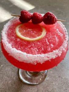 A vibrant fuchsia Raspberry Lemon Drop Cocktail in a chilled coupe glass with beads of condensation and fine ice crystals.