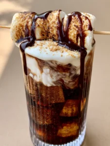 Close up of a Campfire Dirty Soda with cream swirling into dark cola and square ice cubes.