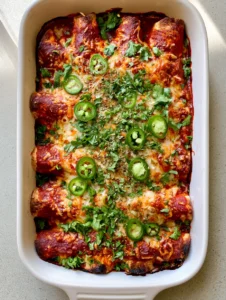 Close-up top-down view of six neatly rolled High-Protein Chicken Enchiladas in a white dish with toasted cheese spots and fresh cilantro. (High-Protein Chicken Enchiladas)