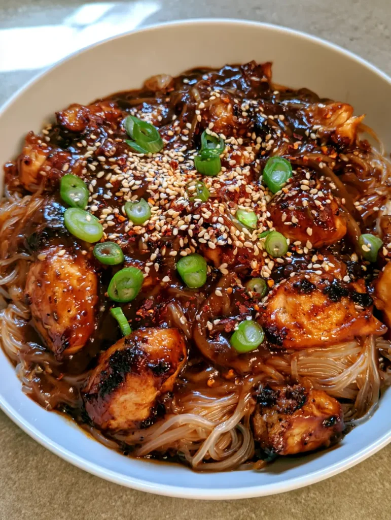 Detailed view of long translucent noodles drenched in a thick dark mahogany sauce with ivory sesame seeds.