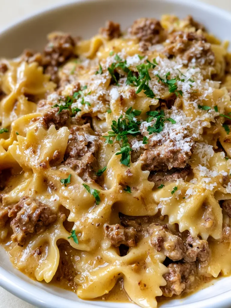 A handheld kitchen photo of bowtie pasta with ground beef, parmesan cheese, and parsley flakes. (Creamy Garlic Parmesan Beef Bowtie Pasta)