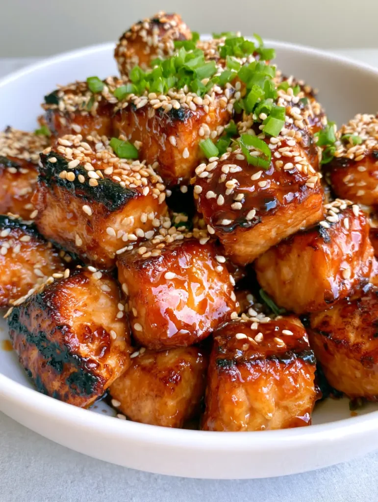 Honey Garlic Salmon Bites: The Ultimate Sticky, Crispy, and Flaky 15-Minute Dinner 1 Detailed view of seared golden-brown charred edges on uniform salmon cubes with toasted sesame seeds and vibrant green scallions. (Honey Garlic Salmon Bites)