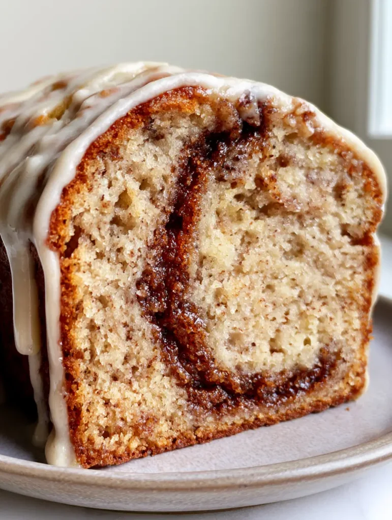 Cinnamon Roll Banana Bread with a Thick Caramelized Sugar Swirl 1 A thick white sugar glaze dripping down the side of a golden-brown Cinnamon Roll Banana Bread loaf.