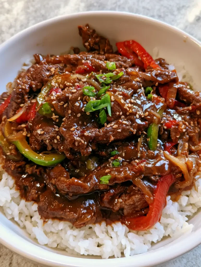 Close-up of tender browned beef strips and wilted bell peppers in a dark savory sauce. (Slow Cooker Pepper Steak)