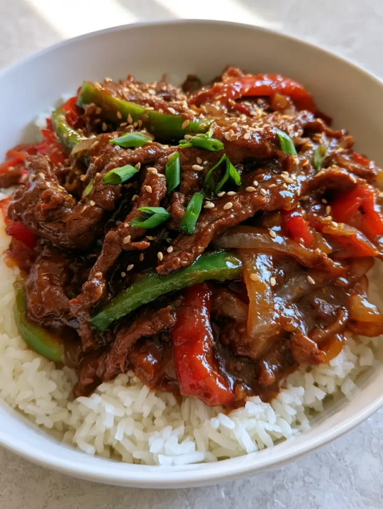 Slow Cooker Pepper Steak: Tender Beef and Glossy Savory Sauce 1 A smartphone photo showing a bowl of pepper steak with sesame seeds and green scallions garnish.