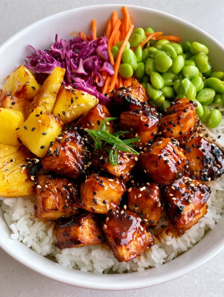 Close up of glossy teriyaki chicken cubes sprinkled with black and white sesame seeds in a Hawaiian Chicken Bowl.