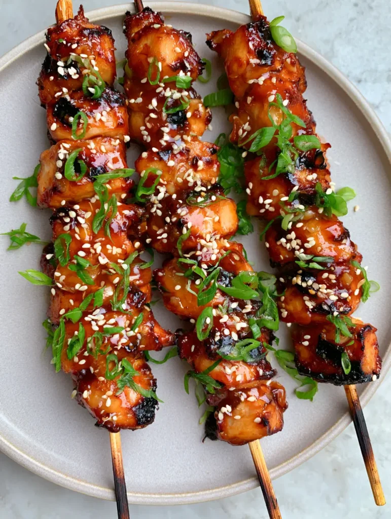 Honey Garlic Chicken Skewers: The Ultimate Sticky and Charred Grilling Recipe 2 Top-down close-up of three Honey Garlic Chicken Skewers resting on a grey ceramic plate with sesame seeds and scallions.