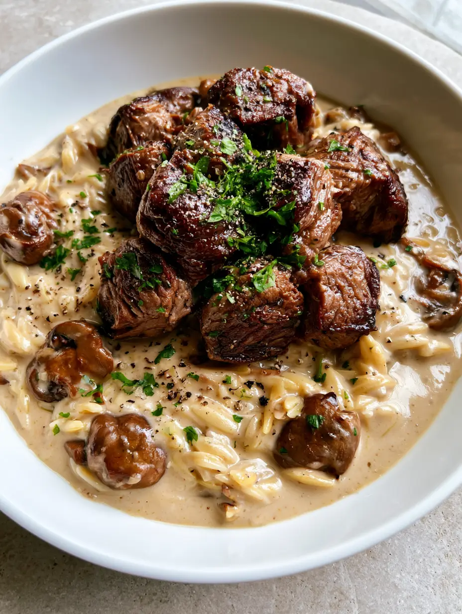 Steak Bites with Mushroom Orzo showing seared beef cubes on creamy pasta in a white bowl under natural light.