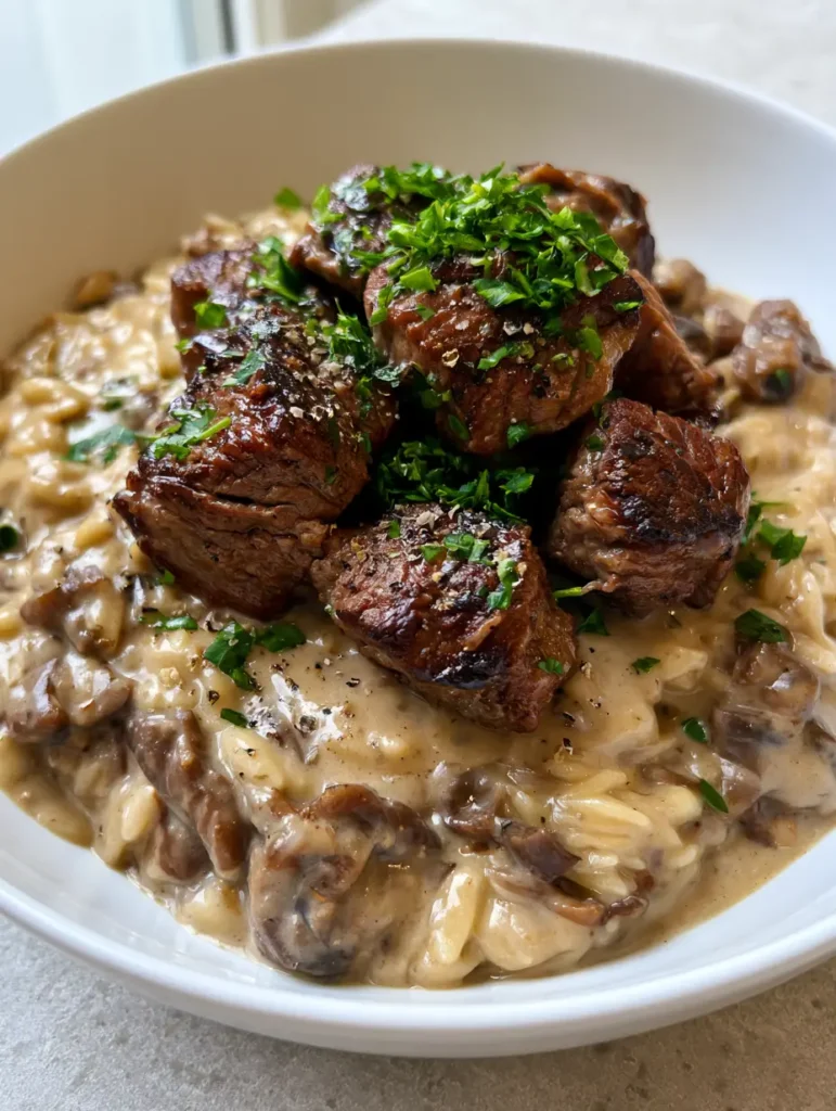 Close-up of caramelised steak bites and sliced brown mushrooms in a thick beige sauce.